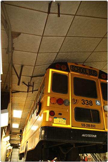 A school bus pushing into the garage ceiling lifting the ceiling panels