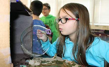 student blowing bubbles into a dark box to see them glow