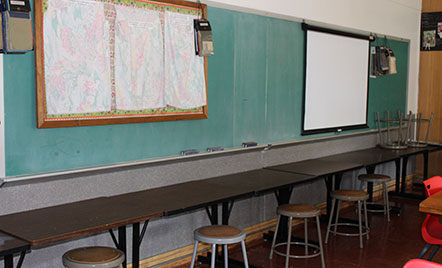 Chalkboard on a wall with old tables and stools in an old classroom