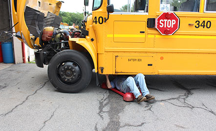 mechanic's legs sticking out from under a bus being worked on outside on the pavement