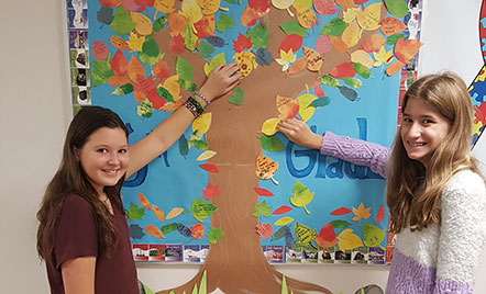 two student putting paper leaves on the paper tree