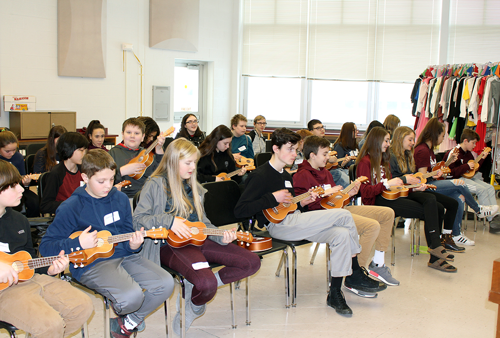 students sitting in chairs playing ukuleles