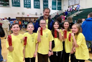 six students wearing matching yellow shirts and one adult holding winner ribbons