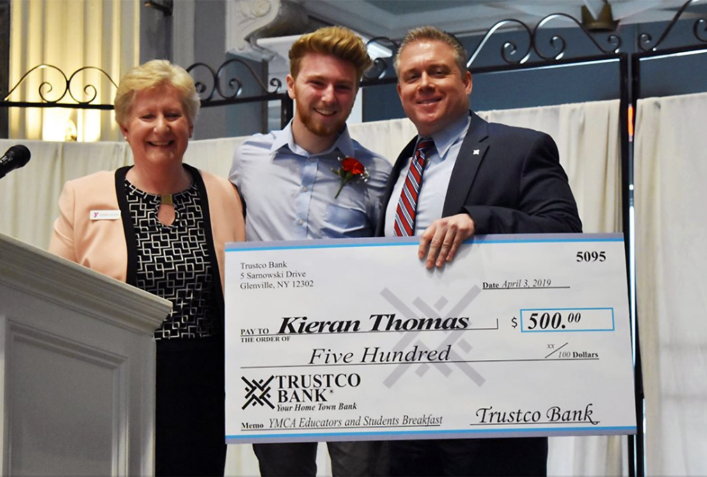 student standing with two adults holding an oversized check