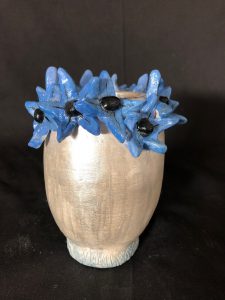 tan vase sculpture with blue and black flowers along the top rim