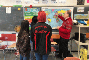 adult pointing to a map with three students watching