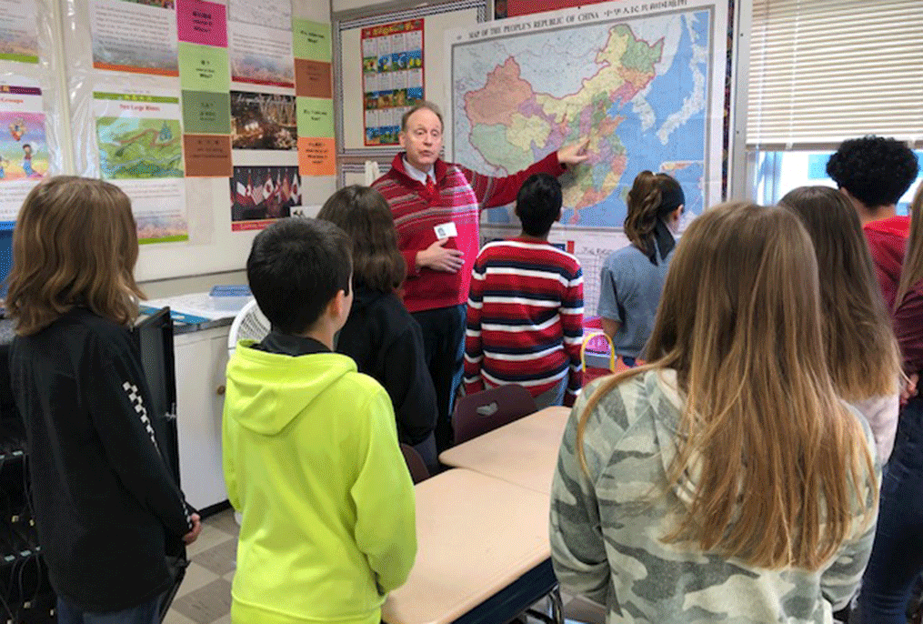 adult taking to students in front of a map