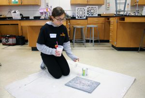 student holding a smoothie and painting on a canvas