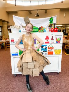 student standing in a costume next to her artwork