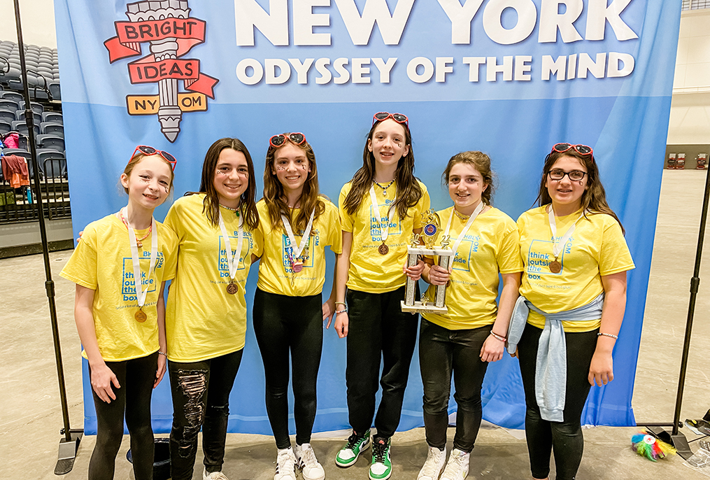students wearing matching yellow shirts standing by the Odyssey of the Mind state banner
