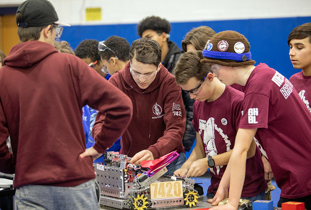 students all wearing maroon team shirts working on a robot on a table