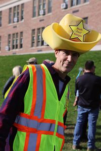 A person wearing a safety vest and an oversized foam cowboy hat