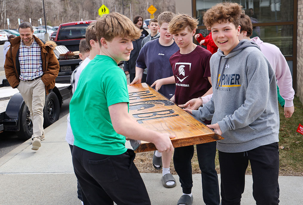 Middle school students holding a wooden sign.
