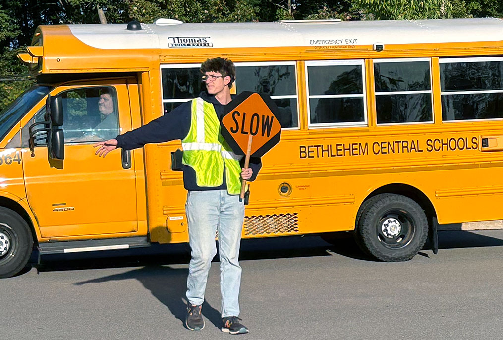 A student holding a slow sign in front of a school bus.