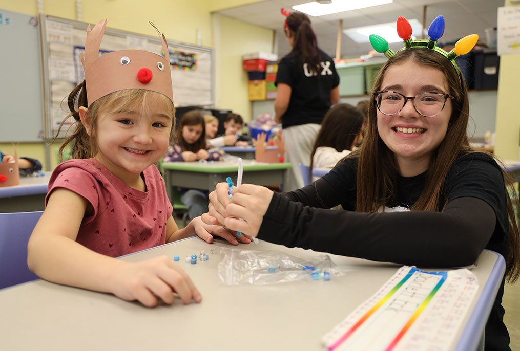 A high school student working with an elementary school student on a Christmas project.