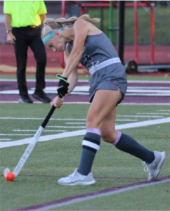 student hitting an orange ball with a field hockey stick