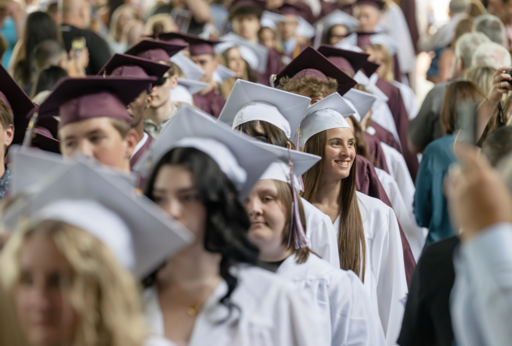 Students walking down the isle at BHBL graduation in maroon and white caps and gowns.