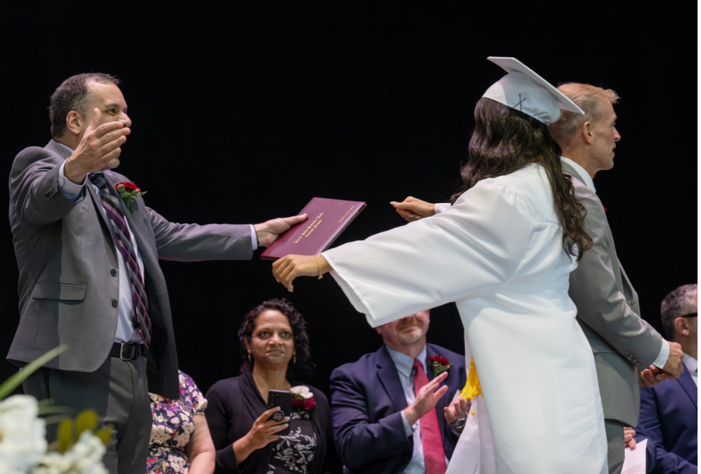 A student in a white cap and gown going to hug their parent at graduation.