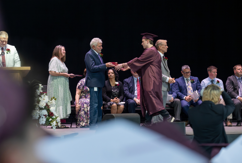 A student in a maroon cap and gown getting their diploma at BHBL graduation.