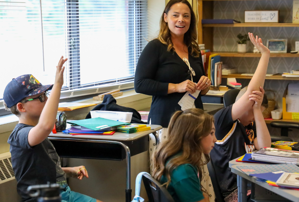 Students raising their hands with a teacher in the room