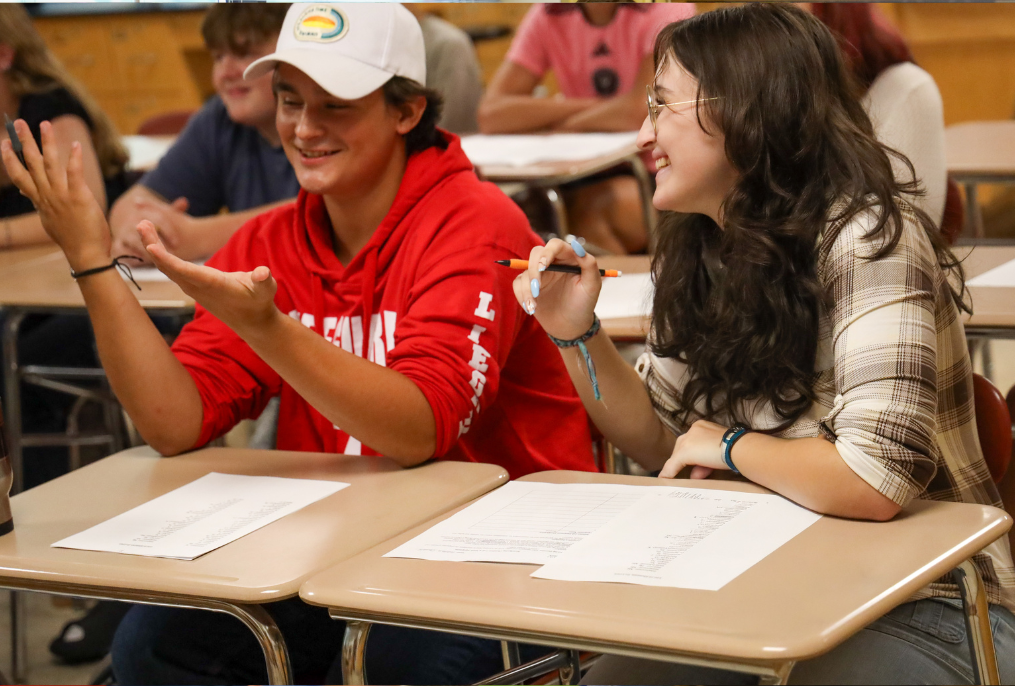 Students in a red sweater and flannel shirt in a classroom.