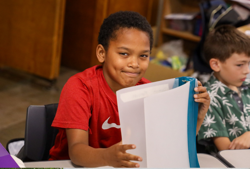 A student smiling holding his binder at school