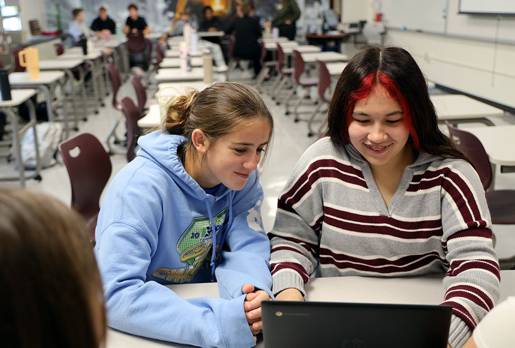 two students leaning in toward each other to view a laptop computer screen