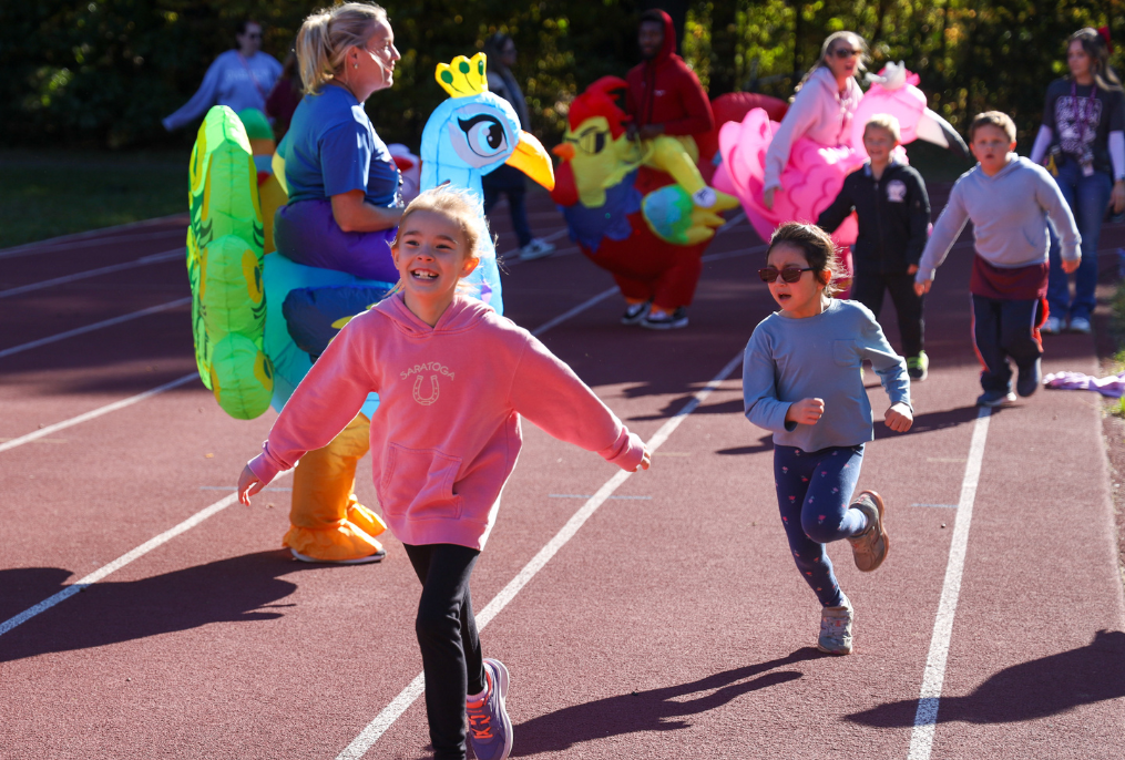 Two students running on a track with a teacher in a costume at Pashley Elementary School