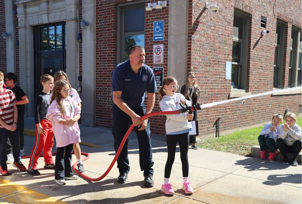 A student at Stevens Elementary School is using a fire hose with a firefighter.